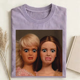 Folded purple t-shirt with a graphic of two dolls on a light background