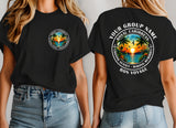 Two women modeling black graphic T-shirts, showing both front and back views. The front has a small circular tropical sunset print on the left chest, and the back has a large matching circular print with the text 'YOUR GROUP NAME', 'ROYAL CARIBBEAN', 'GRASSY SUNSET', 'MAKING MEMORIES', and 'Bon Voyage'.