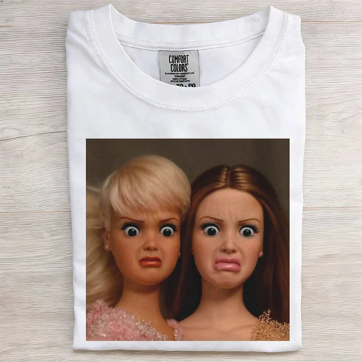 White t-shirt with a graphic of two dolls on a wooden surface